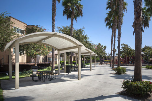 Outdoor seating areas under arched cabanas with grills, cement ground, and palm trees